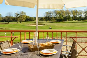 A dining table with plates, glasses, and a bread basket on a wooden deck with a view of a golf course. - Stylish coastal apartment with shared pool (Fréhel)