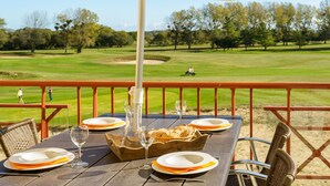 Ein Esstisch mit Tellern, Gläsern und einem Brotkorb auf einer Holzterrasse mit Blick auf einen Golfplatz.