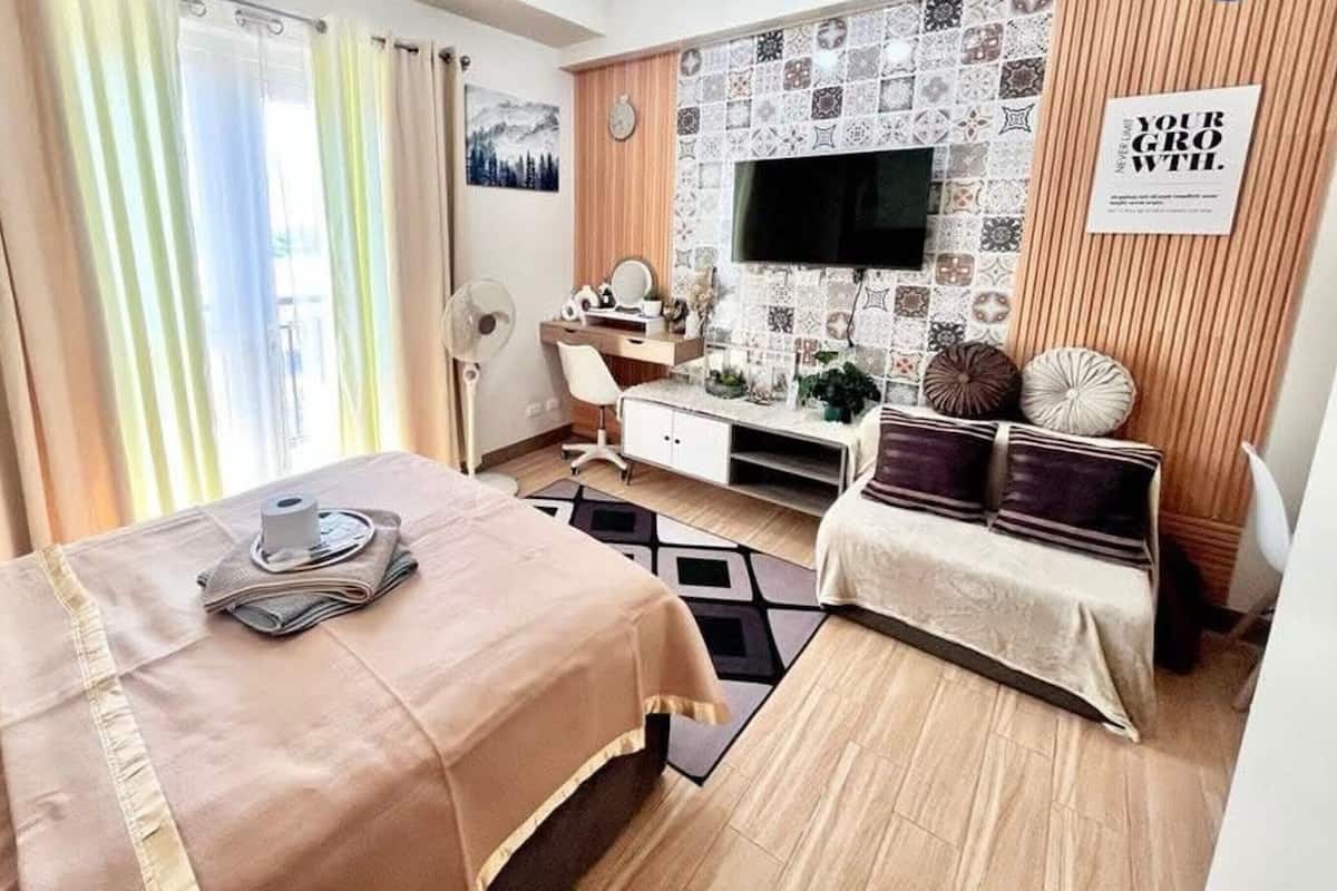 Una habitación de hotel con cama, escritorio, silla, televisor y una pared con diseño decorativo.