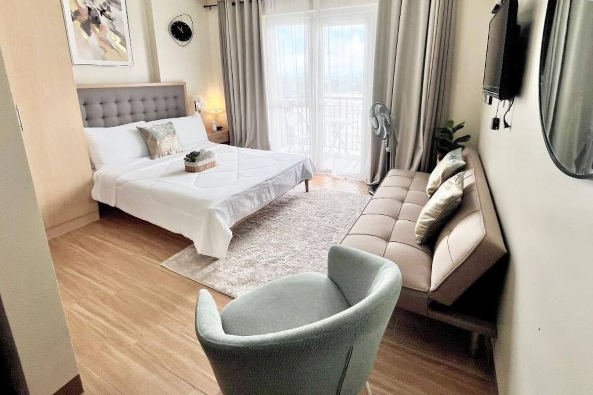 A bedroom with a bed, a sofa, a chair, a TV, and a window with curtains.