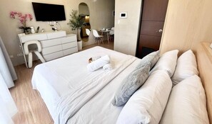 A hotel room with a bed, a desk, a chair, a TV, and a door.