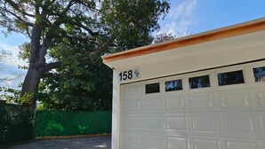 A white garage with the number 158, a green fence, and a tree in the background. - Apartment in San Salvador (San Salvador)