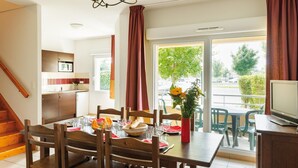 A dining area with a table set for four, a vase with flowers, and a television on a stand. - Duplex Maisonette in Dordogne (Bergerac)