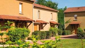 A row of beige buildings with red-tiled roofs, surrounded by greenery and a clear sky. - Duplex Maisonette in Dordogne (Bergerac)
