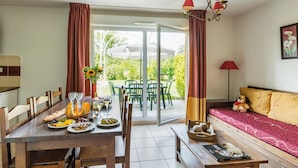 Un coin repas avec une table mise pour le repas, un canapé avec un ours en peluche, et une porte-fenêtre coulissante donnant sur une terrasse extérieure.