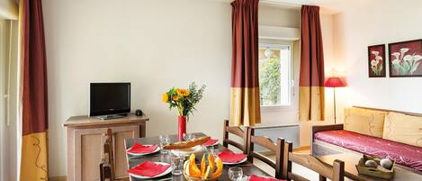 A dining area with a table set for two, a television, and a sofa.