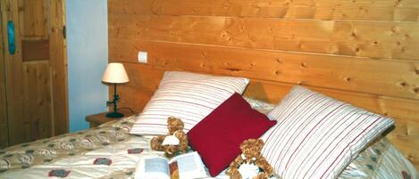 A wooden-paneled room with a bed, pillows, a lamp, and a teddy bear.
