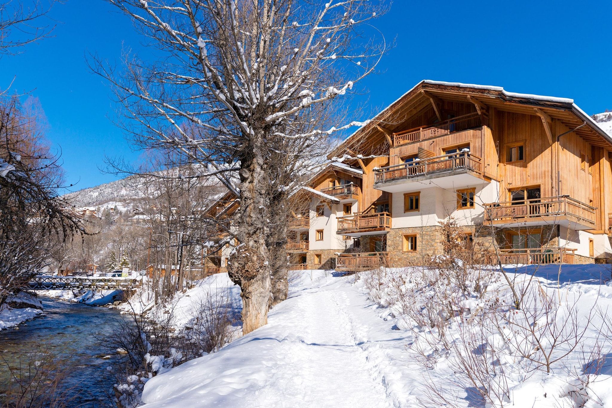 Un chalet en bois doté de plusieurs balcons, avec des fondations en pierre et surplombant un paysage enneigé.