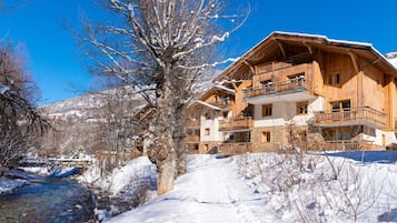 Un chalet en bois doté de plusieurs balcons, avec des fondations en pierre et surplombant un paysage enneigé.