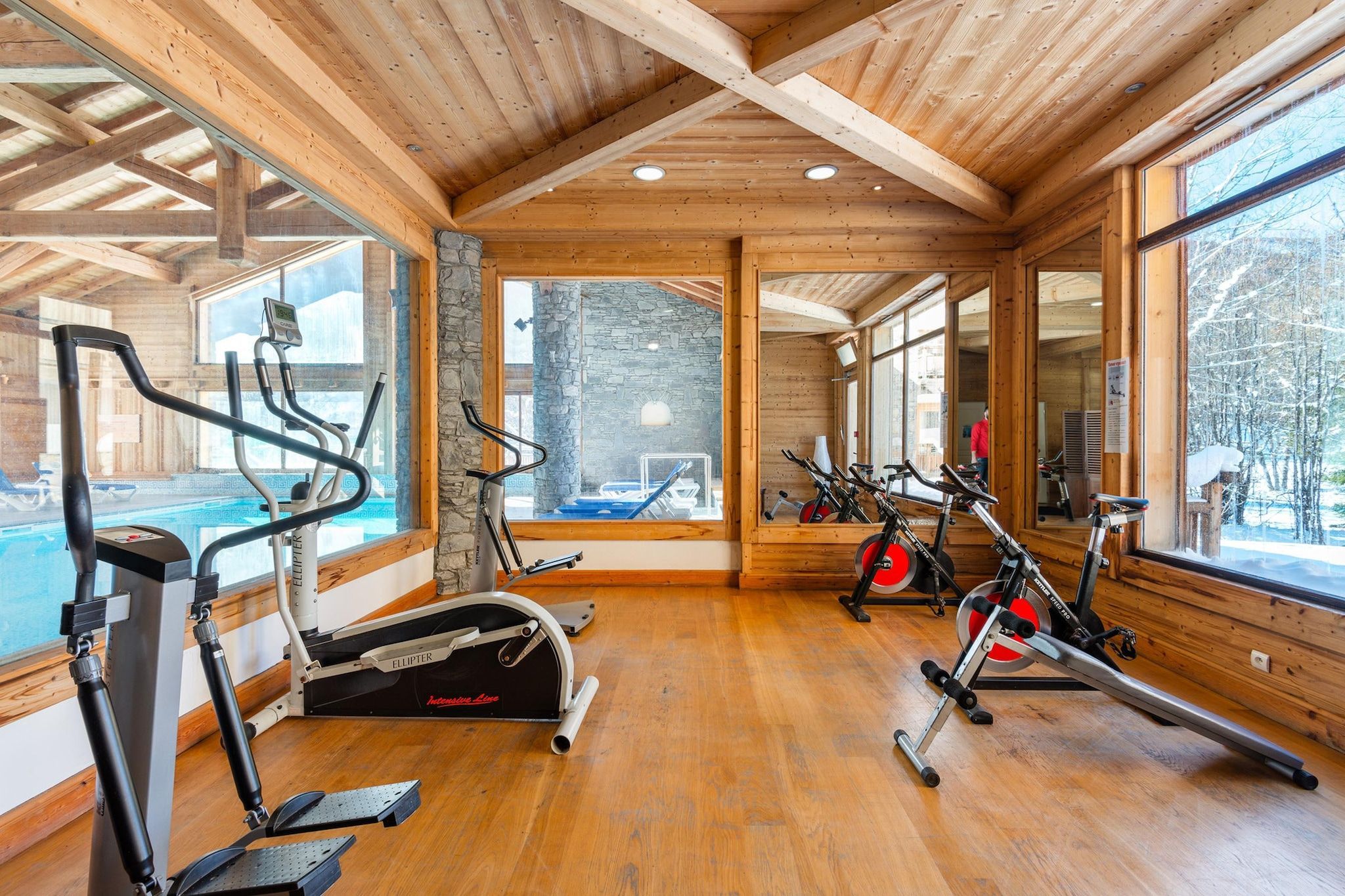 A gym with various exercise equipment, large windows, and wooden interior.
