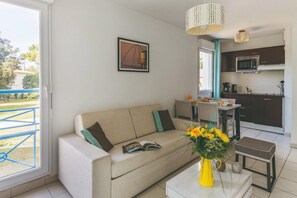 A modern living room with a sofa, coffee table, and a dining area with chairs. - Duplex Retreat near the Beach (Saint-Palais-sur-Mer)