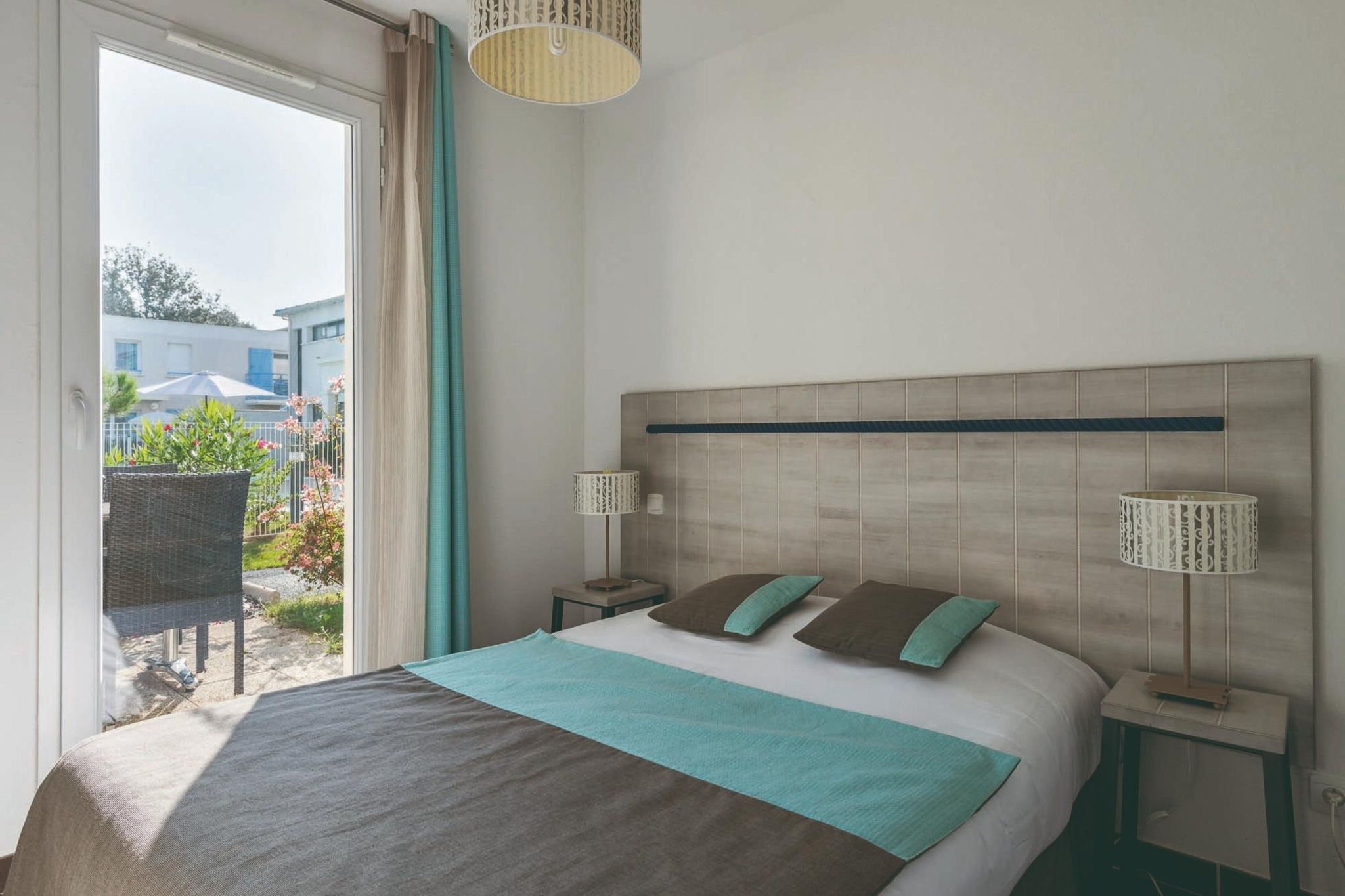 Quarto com cama, duas mesas de cabeceira, janela com cortinas e vista para o exterior.