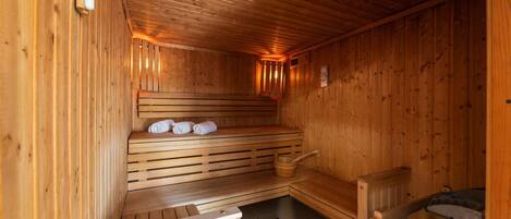 A wooden sauna with benches, a bench with towels, a wooden bucket, and a sauna heater.