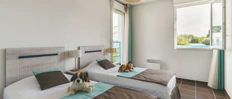 A hotel room with two beds, a window with curtains, a hanging lamp, and a stuffed toy on one bed.