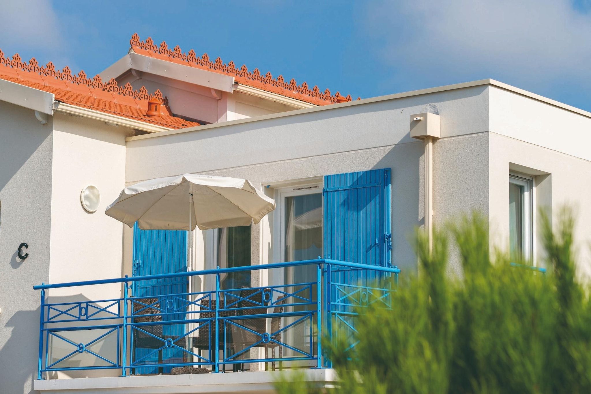 A building with a balcony, a white exterior, and a red-tiled roof.