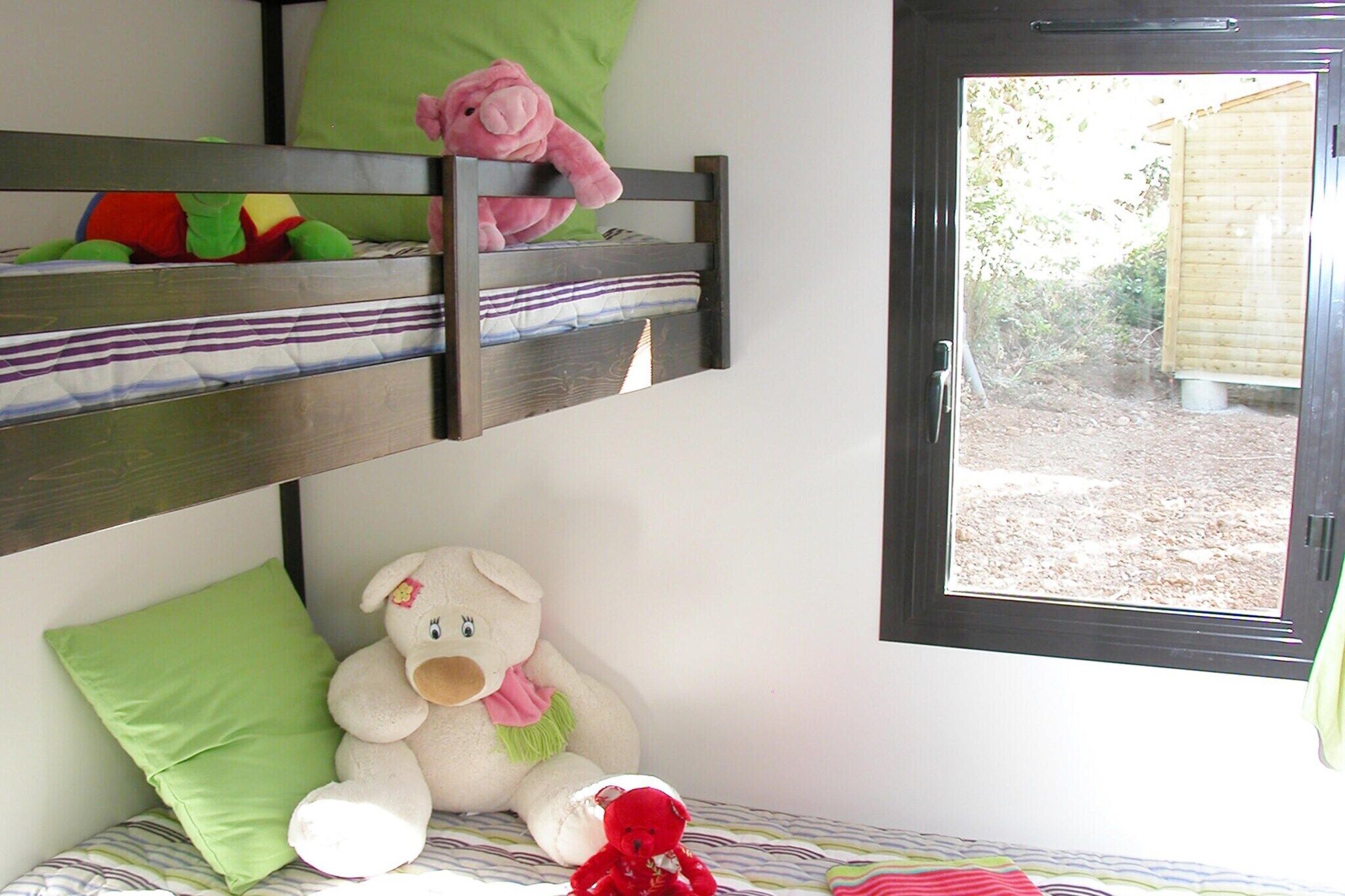 Un lit superposé avec une fenêtre, un ours en peluche et un oreiller vert.