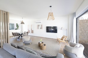 Ein modernes Wohnzimmer mit Sofa, Sesseln, einem Fernseher und einem Essbereich.