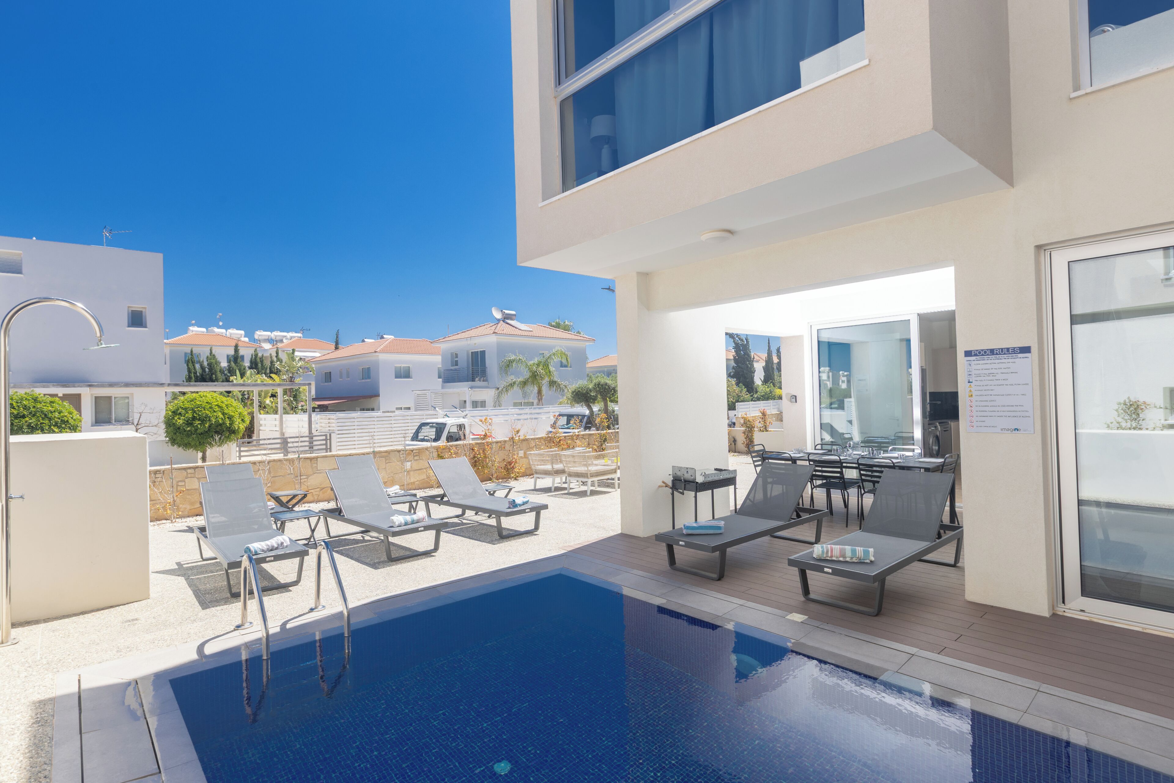 A modern outdoor pool area with lounge chairs, a pool table, and a view of neighboring buildings.