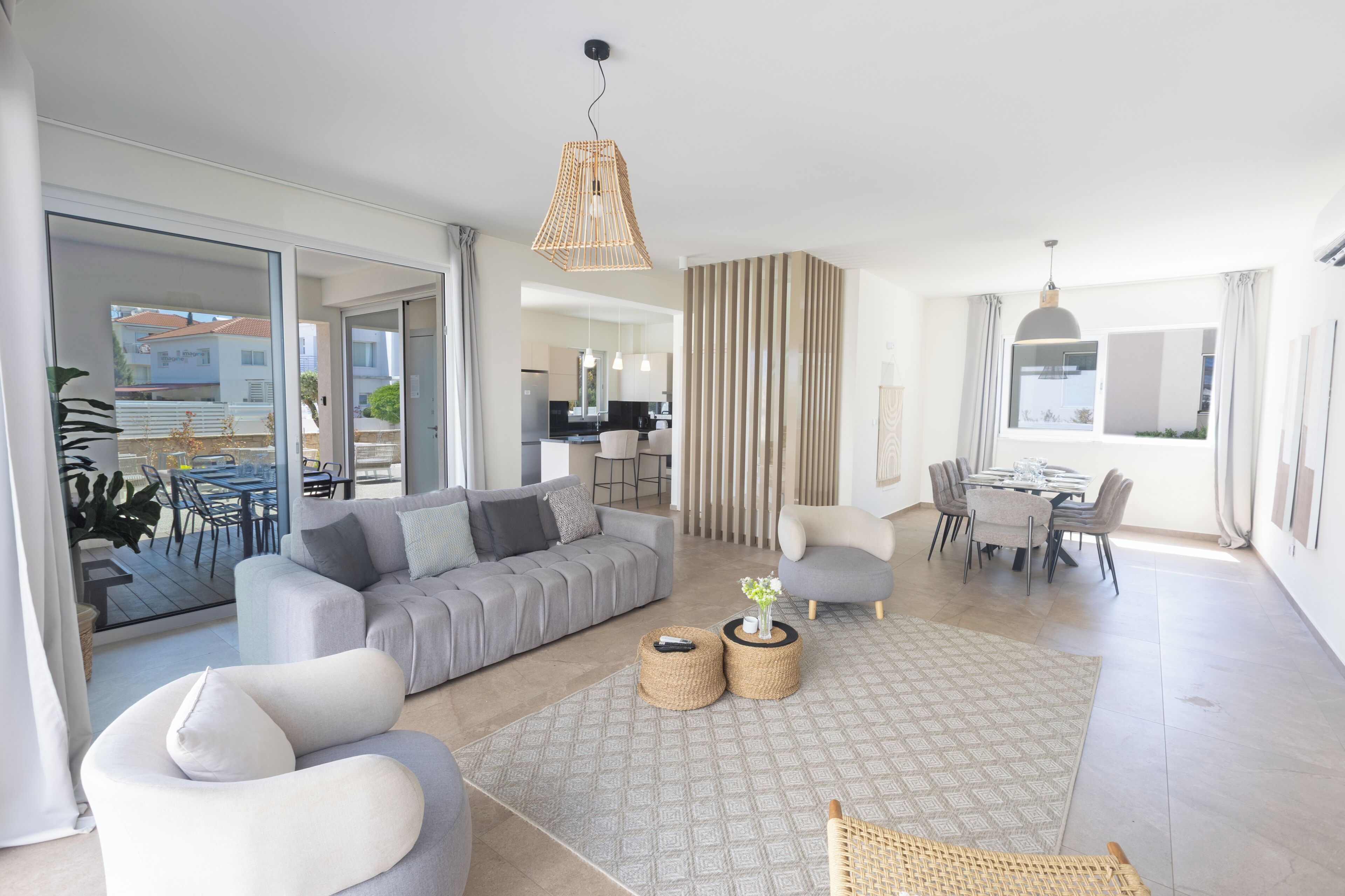 A modern living room with a grey sofa, a dining table, and a kitchen in the background.