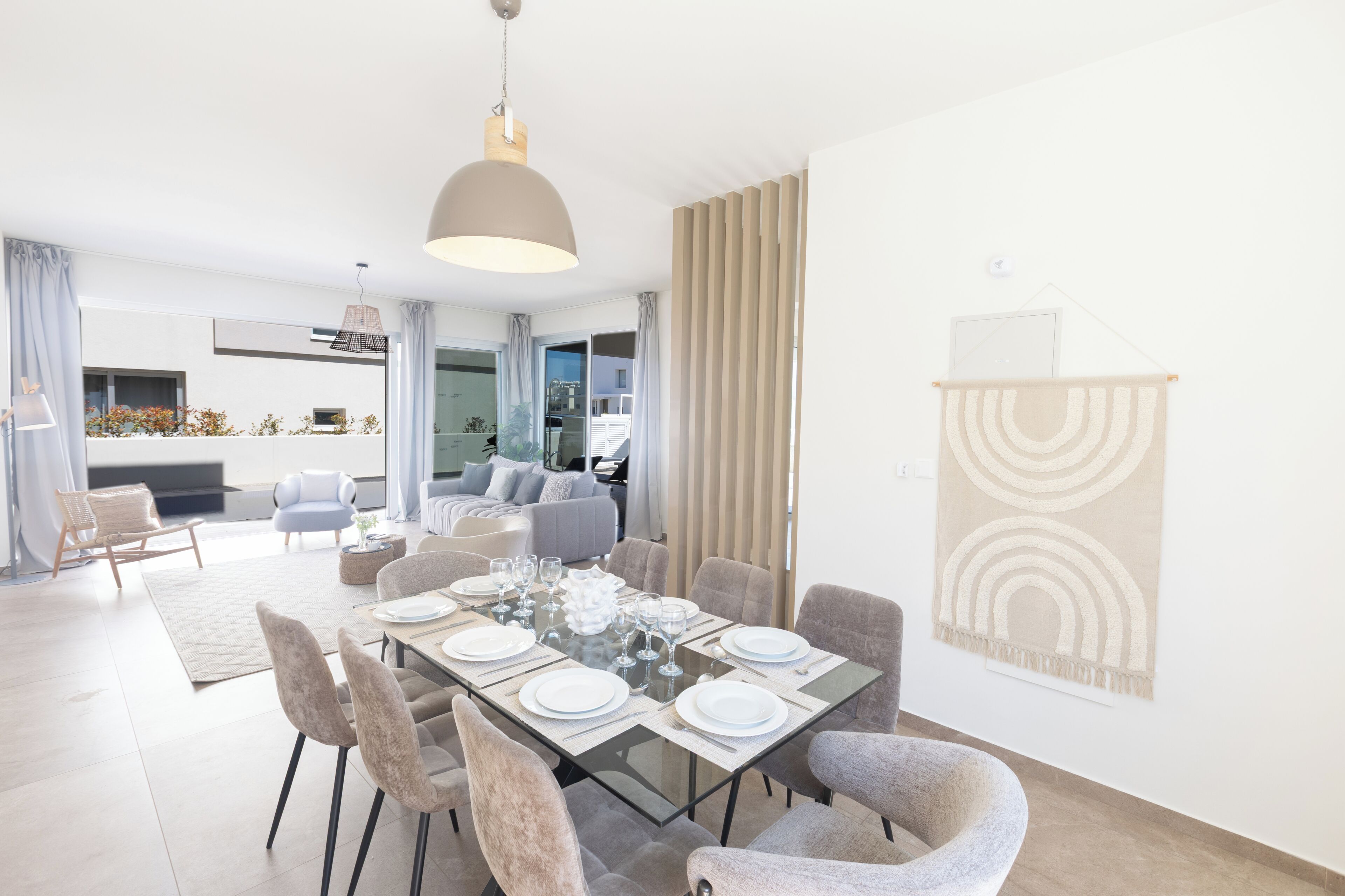 A modern dining area with a glass table, chairs, and a pendant light.