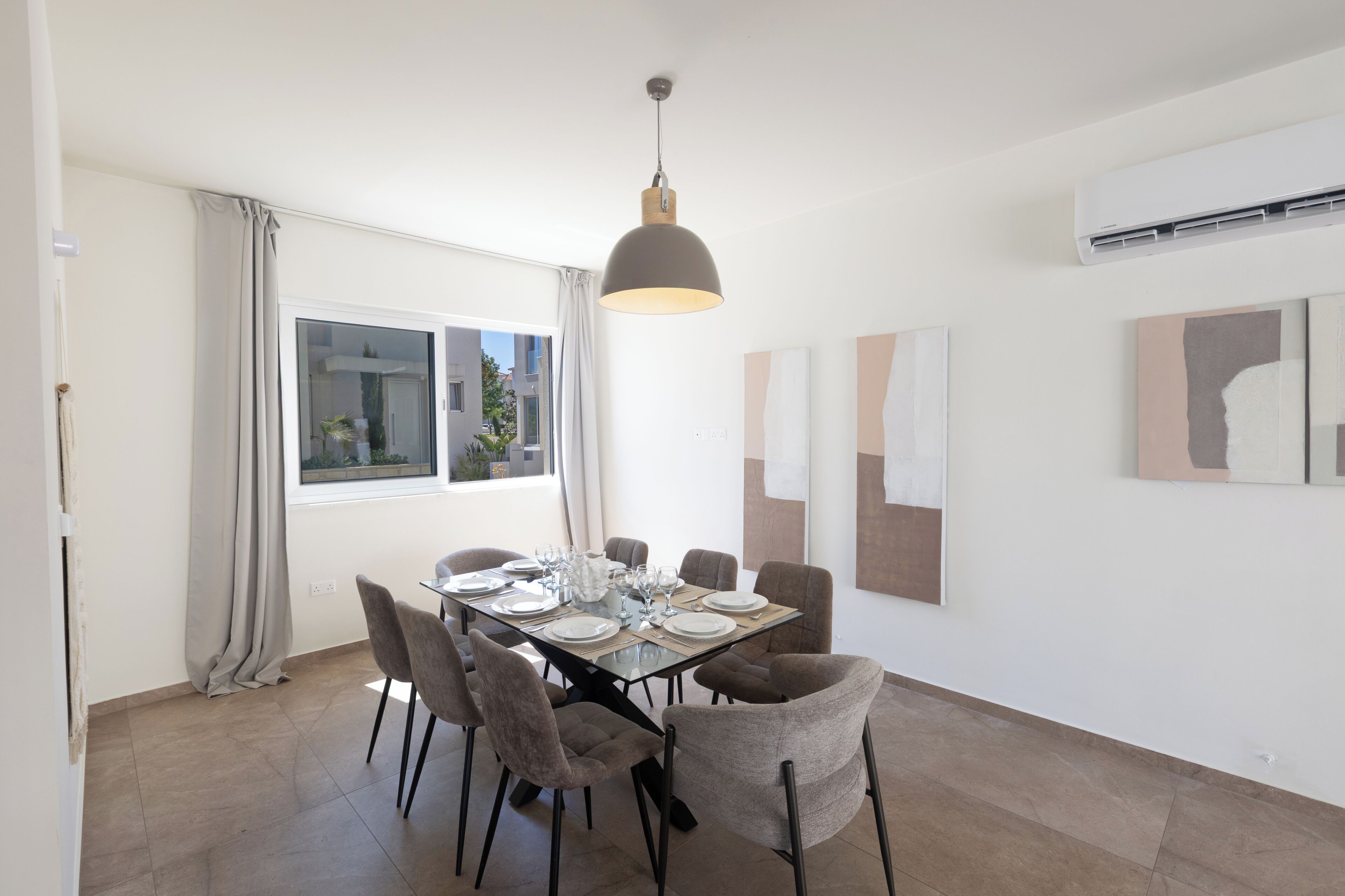 A dining area with a table set for six, six chairs, a hanging pendant light, and artwork on the walls.