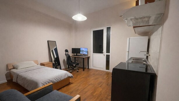 A bedroom with a bed, desk, computer, and a kitchenette. - Casa Katerina studio apartment (Chania)