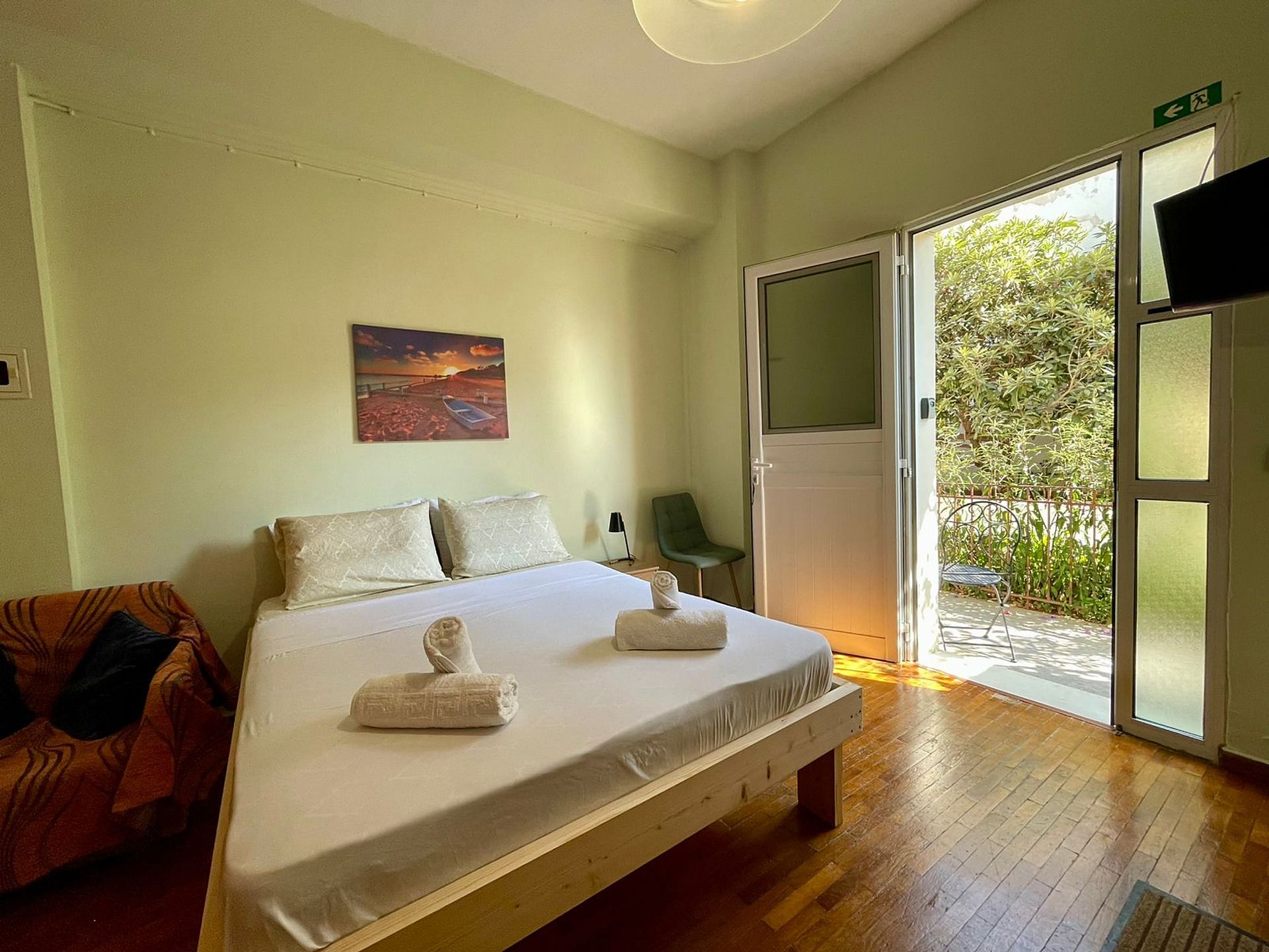 A room with a bed, a chair, a painting, and a door leading to a balcony.