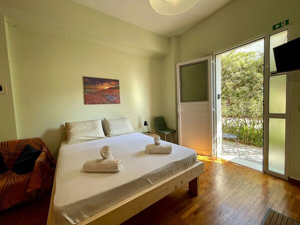 A room with a bed, a chair, a painting, and a door leading to a balcony. - Casa Katerina studio apartment (Chania)
