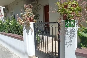 A gated entrance with a metal gate, a white wall, and a potted plant with green leaves. - Casa Katerina studio apartment (Chania)