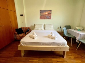 A bedroom with a bed, two pillows, a chair, a table, and a painting on the wall. - Casa Katerina studio apartment (Chania)