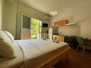A bedroom with a bed, a bench, a desk, and a kitchenette. - Casa Katerina studio apartment (Chania)