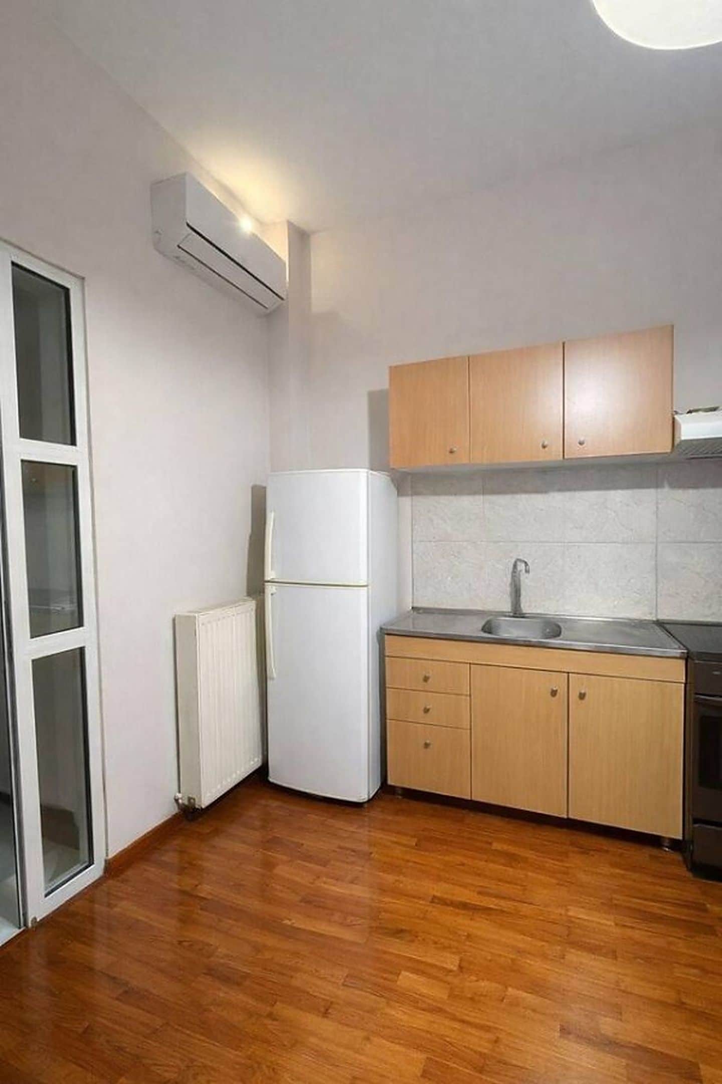 Eine kleine Küche mit Kühlschrank, Spüle, Holzschränken und Heizkörper.
