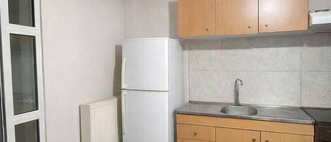 Eine kleine Küche mit Kühlschrank, Spüle, Holzschränken und Heizkörper.
