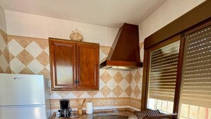 A compact kitchen with a refrigerator, stove, sink, and wooden cabinets. - Casa Zerimar       . (Conil de la Frontera)