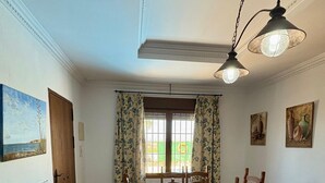 A dining area with a table and chairs, a television, and a ceiling light fixture. - Casa Zerimar       . (Conil de la Frontera)