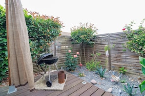 A wooden deck with a grill, a metal pot, and a small garden with plants and a fence.