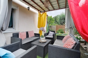 An outdoor patio with wicker furniture, a table with a plant, and a yellow curtain.