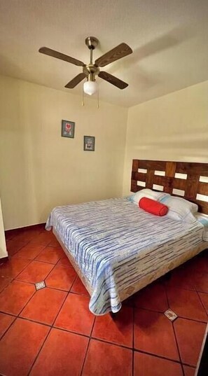 Une chambre à coucher avec un lit, un ventilateur de plafond et un revêtement de sol carrelé.