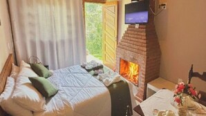 A bedroom with a bed, a TV mounted on a brick wall, and a fireplace. - POUSADA ALL GREEN (Camanducaia)