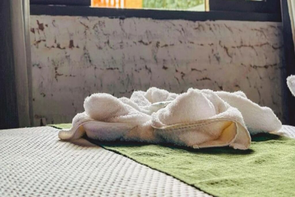 A bed with a white blanket and a green towel on a textured surface.