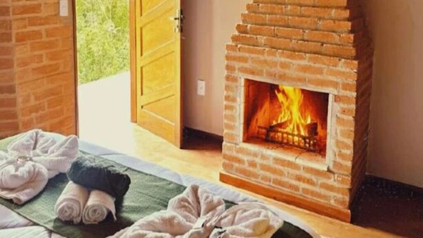 A room with a brick fireplace, towels on the floor, and a wooden door. - POUSADA ALL GREEN (Camanducaia)