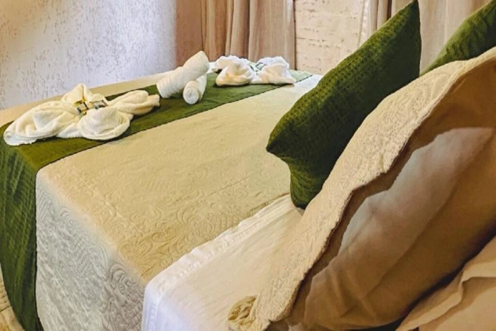 A neatly made bed with a green pillow, a white towel, and a rolled-up towel on a green cloth.