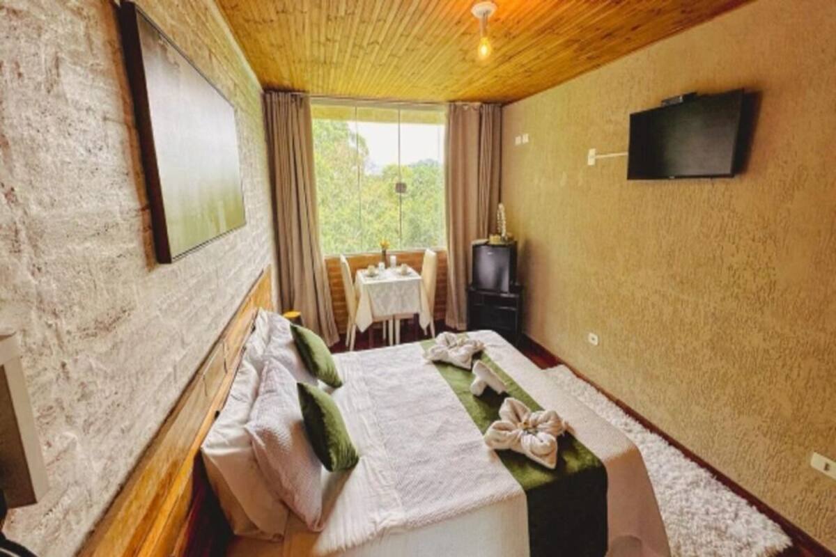 A bedroom with a bed, a TV, a window, and a table with chairs.