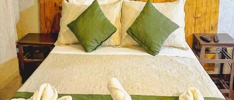 Habitación de hotel con cama, almohadas, mesita de noche, control remoto y toallas sobre la cama.