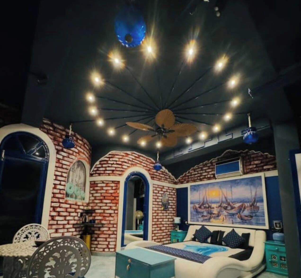 A room with a brick wall, a bed, a ceiling fan, and a painting.