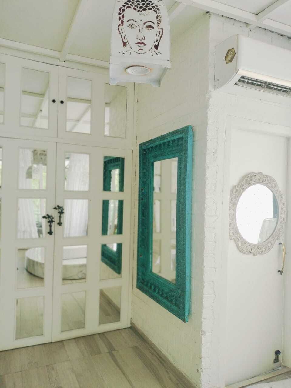 A room with white walls, a teal-framed mirror, a round mirror, and a door with glass panels.