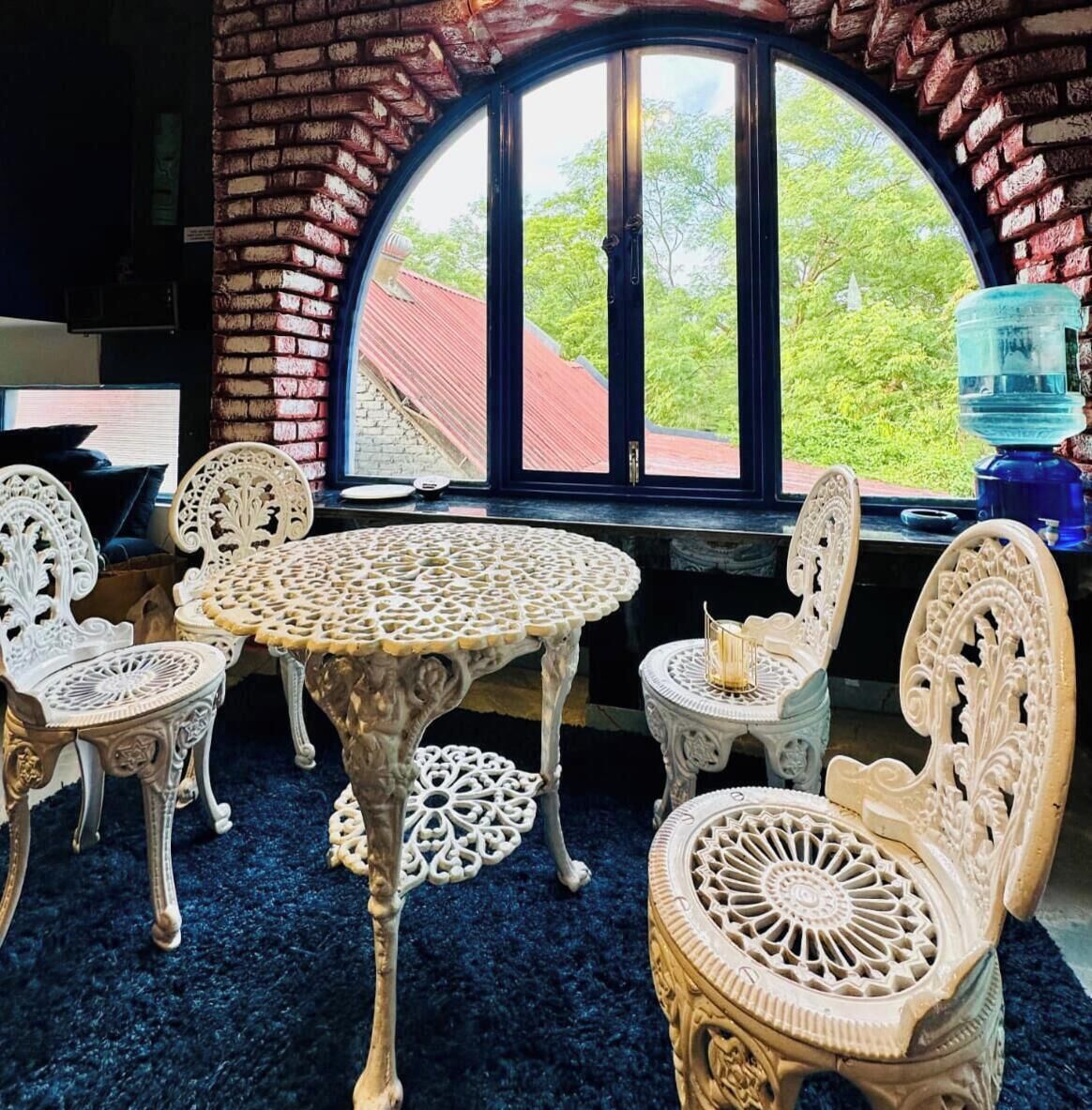 Une pièce dotée d’une table ronde et de chaises richement décorées, d’une grande fenêtre en arc de cercle et offrant une vue sur la verdure environnante.
