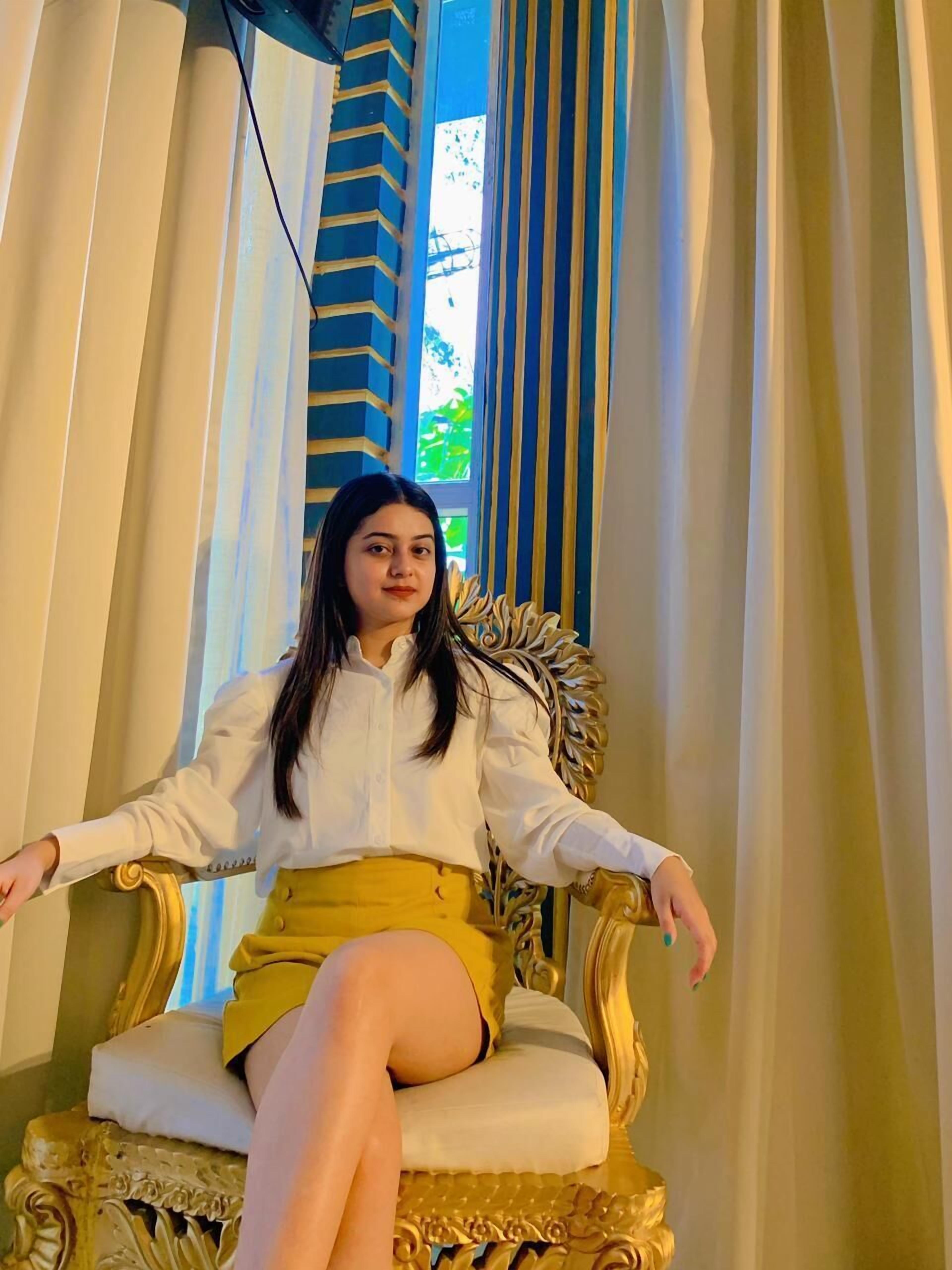 Una persona sentada en una silla decorada, con una ventana al fondo.