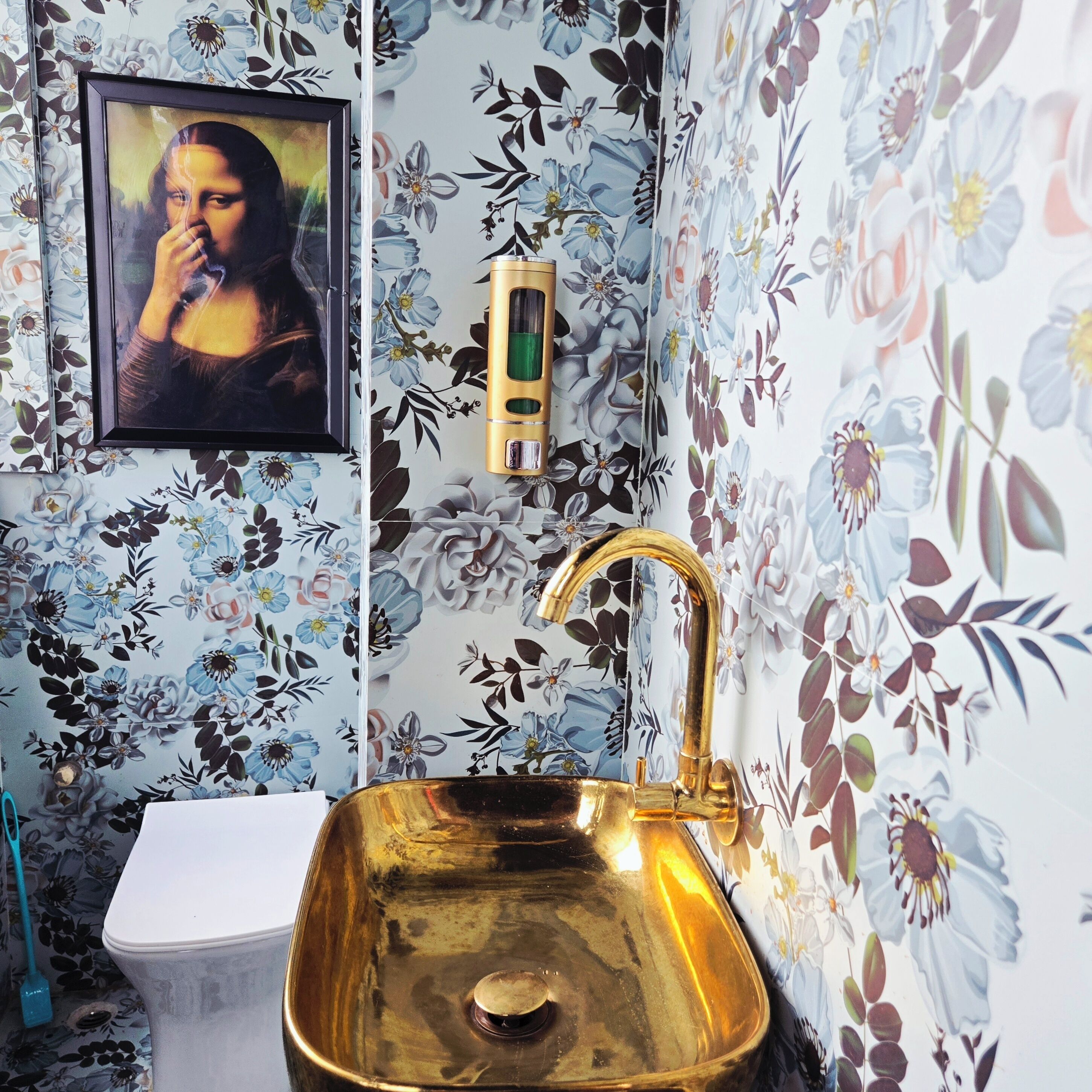 Een badkamer met een gouden wastafel, een toilet en een ingelijst kunstwerk aan de muur.