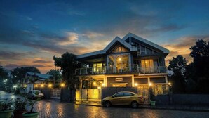 A modern two-story building with a balcony, a car parked in front, and a paved driveway.